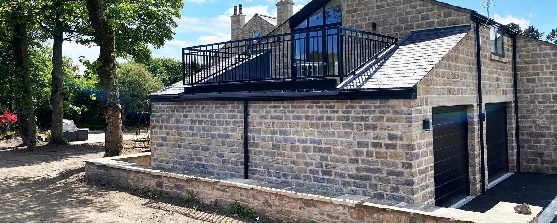 Contemporary stone building with balcony, slate roof and garage doors