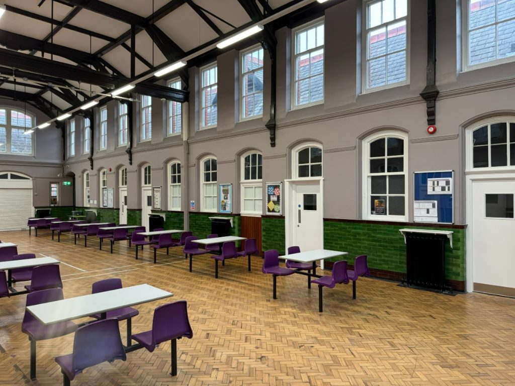 School hall with vaulted timber trusses, green tiling and dining tables